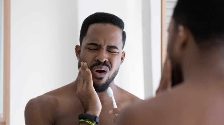 man touching cheek and brushing teeth