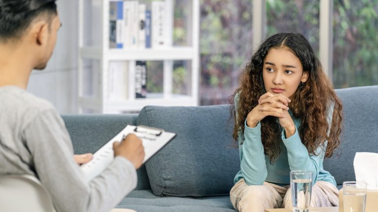 Young woman sits on couch listening to her therapist