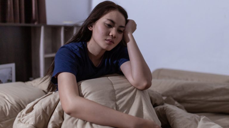 Woman sitting up in bed with hand on head