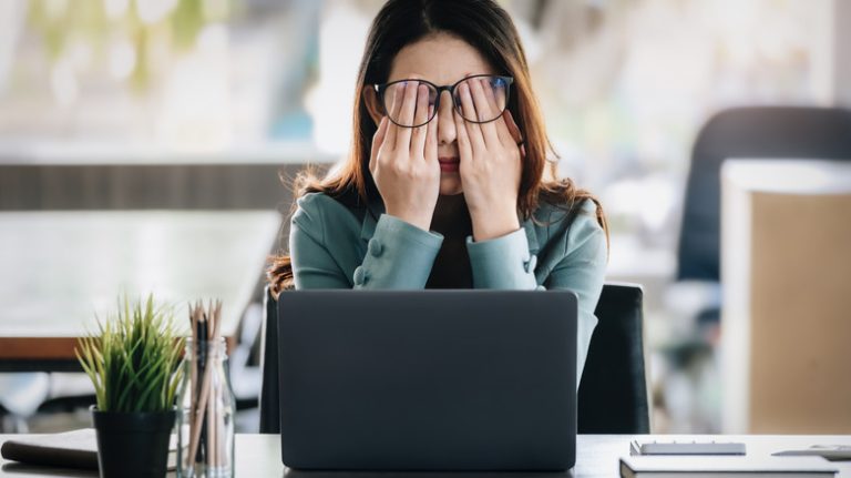 woman rubbing her eyes while sitting in front of a computer