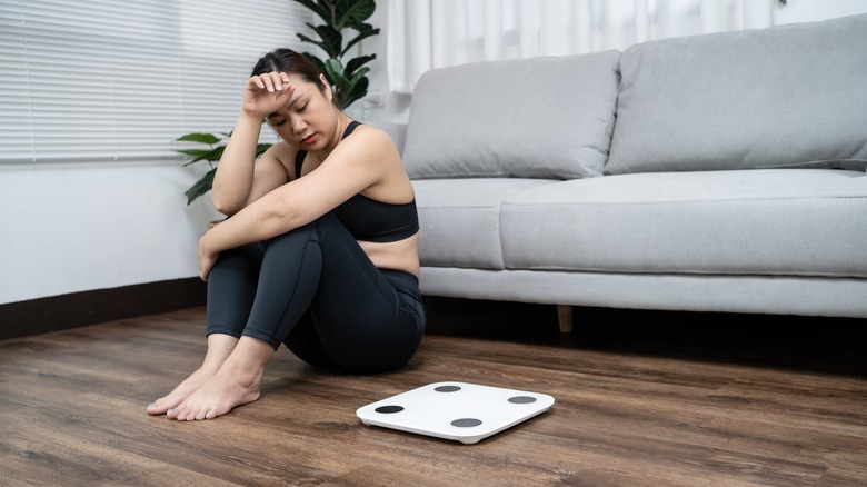 Distressed woman sitting by scale