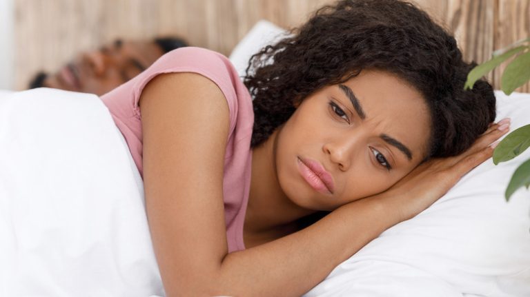 a woman laying in bed next to partner looking sad