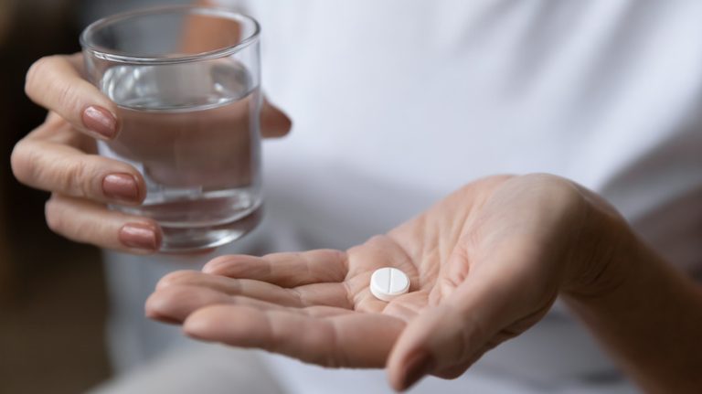 Hand holding pill and glass of water