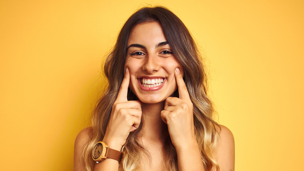 woman smiling, pointing to cheeks