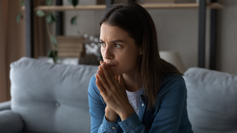 Worried woman sits on sofa