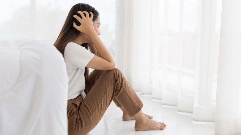 Woman sits on floor, holding her head